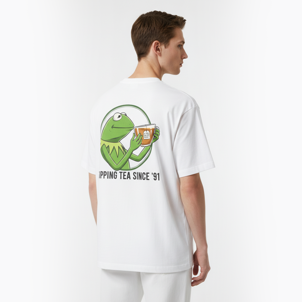 Person wearing a white t-shirt with a graphic of a green frog holding a cup and text on the back.
